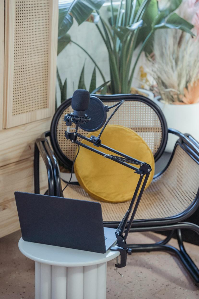 A professional microphone with a pop filter mounted on an arm, positioned in front of a laptop on a table in a home office setting