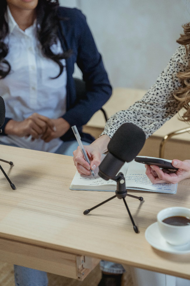 Two people sitting at a table facing a laptop and microphone, engaged in a media recording session.