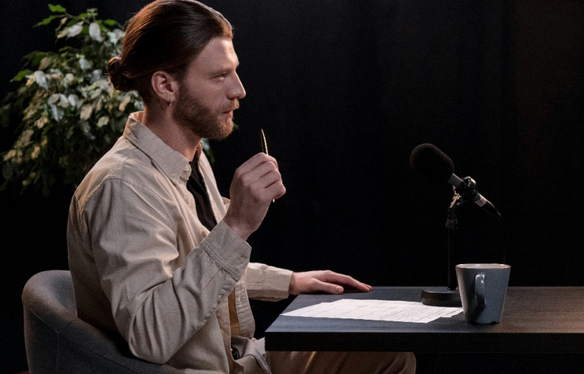 A man sitting at a table with a microphone in front of him, engaged in a podcast interview