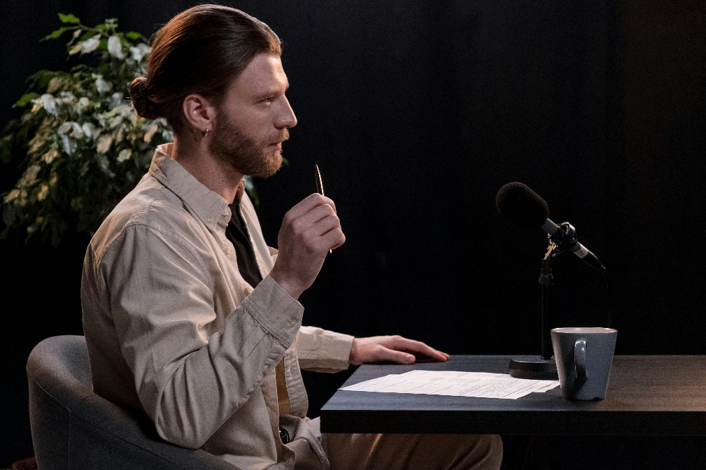A man sitting at a table with a microphone in front of him, engaged in a podcast interview