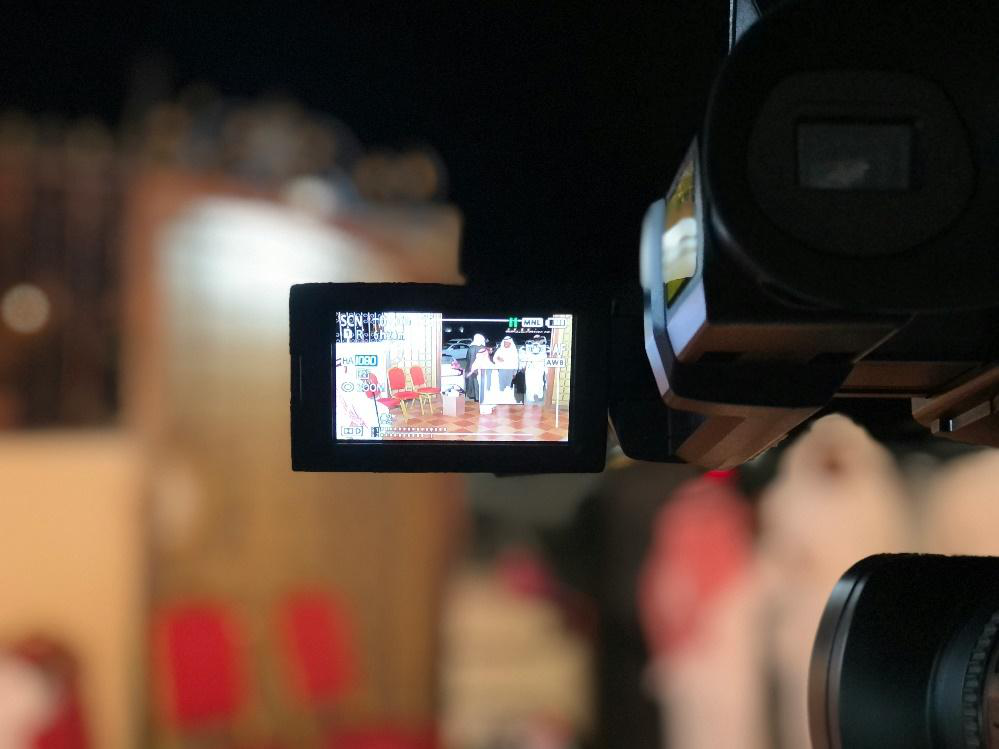 A camera operator filming a scene with two people in the background