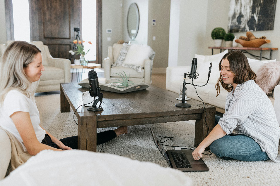 Two women recording a podcast while sitting across a table, using microphones