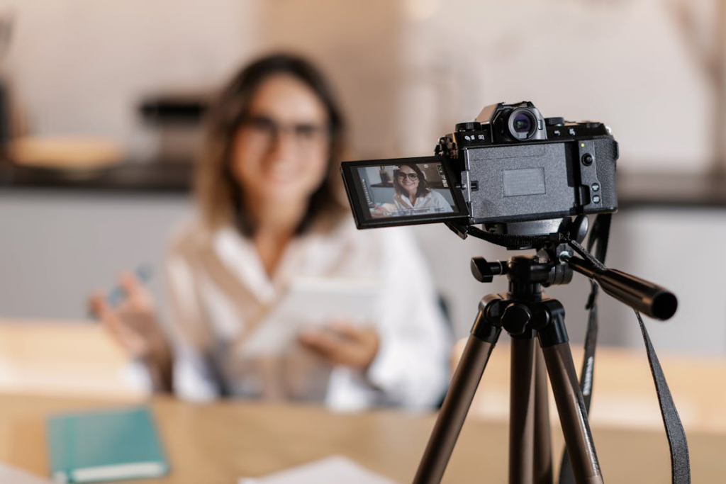 A woman in a white top filming herself with a digital camera setup on a tripod.