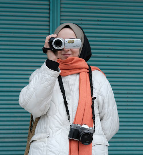 A woman using a Sony Handycam to record video outdoors, focusing intently through the camera lens.