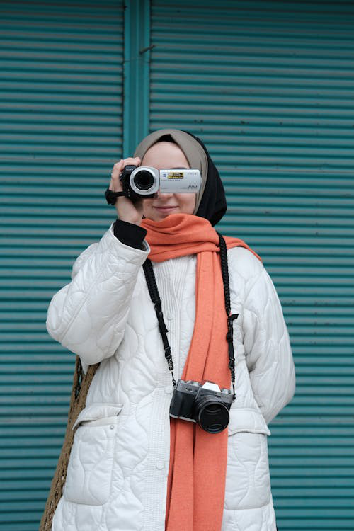 A woman using a Sony Handycam to record video outdoors, focusing intently through the camera lens.